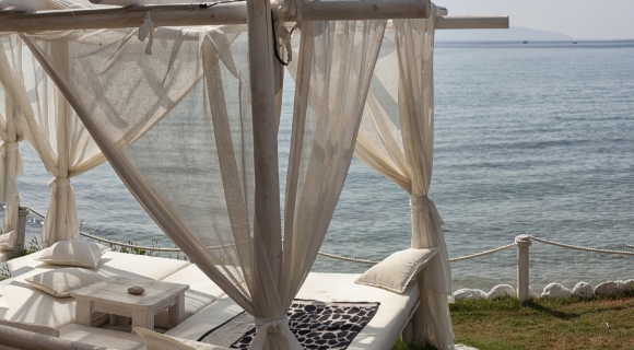 Outdoor-Bett mit transparenten Stoffbahnen und Blick auf das ruhige Wasser an einer Küstenlinie.