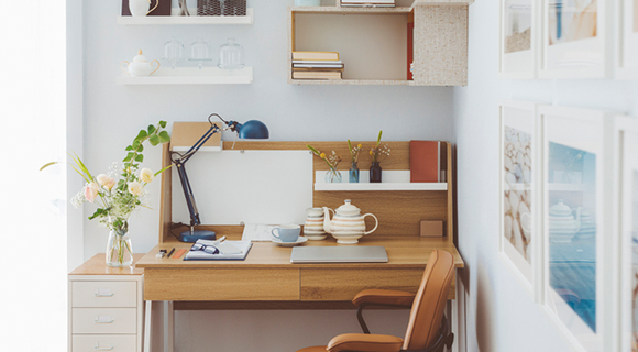 Kleiner Arbeitsplatz mit Holztisch, Lederstuhl und Regal an der Wand.
