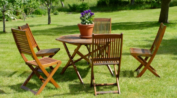 Mehrere Klappst&uuml;hle stehen an einem runden Holztisch auf dem Rasen im Garten.