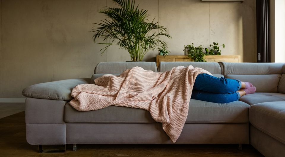 Frau liegt mit Decke über dem Kopf auf einer grauen Schlafcouch