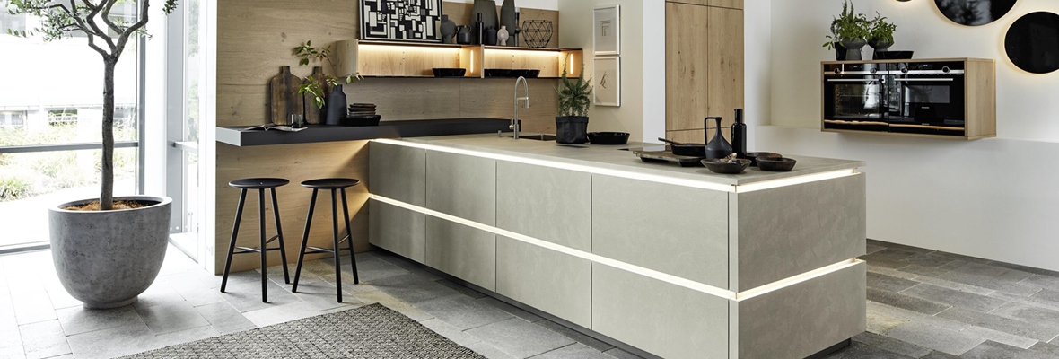 Küche in Betonoptik mit moderner und robuster Gestaltung. Die Küche verfügt über eine zentrale Insel in Betonoptik mit integrierter Beleuchtung, Holzelementen an der Wand und Dekorationen wie Vasen und Kunstwerken. An der Wand befinden sich runde, schwarze Wanddekorationen, die dem Raum einen besonderen Akzent verleihen