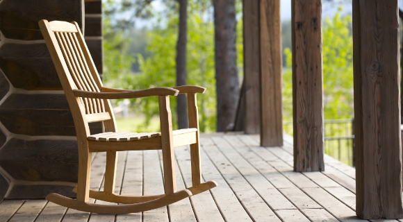 Ein Schaukelstuhl aus Holz steht auf der Veranda eines Hauses.