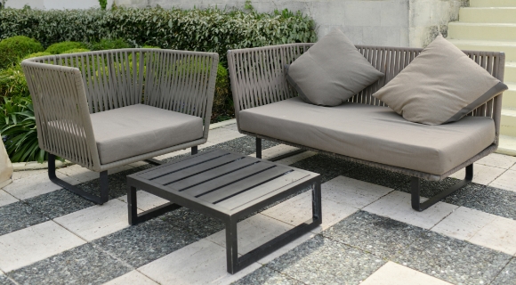 Moderne Gartenm&ouml;bel aus Geflecht mit grauen Polstern und Beistelltisch auf einer Terrasse im Au&szlig;enbereich.