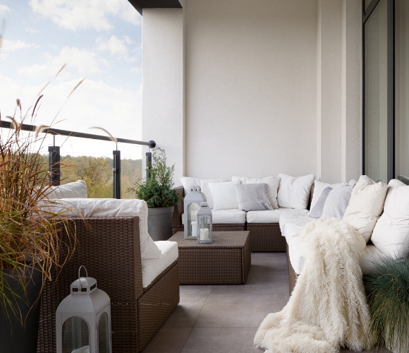 Moderne Balkonlounge mit Ecksofa, Kissen, Decke und Laternen.