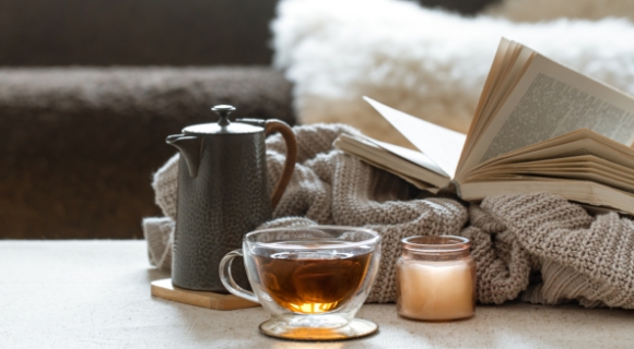 Gemütliche Szene mit einer Tasse Tee, Teekanne und Buch auf einem Tablett – entspannte Atmosphäre im Wohnzimmer.