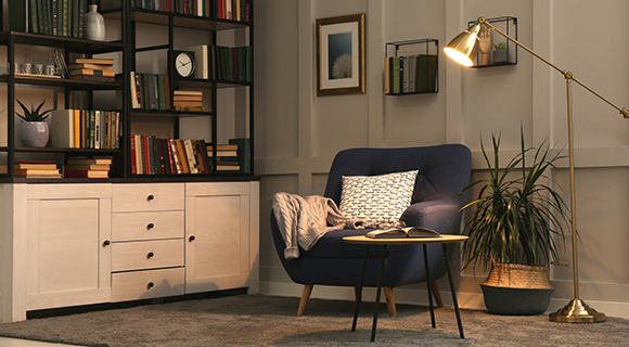 Gemütliche Leseecke mit blauem Sessel, Stehleuchte, Bücherregal, Teppich und Zimmerpflanzen in warmem Licht.