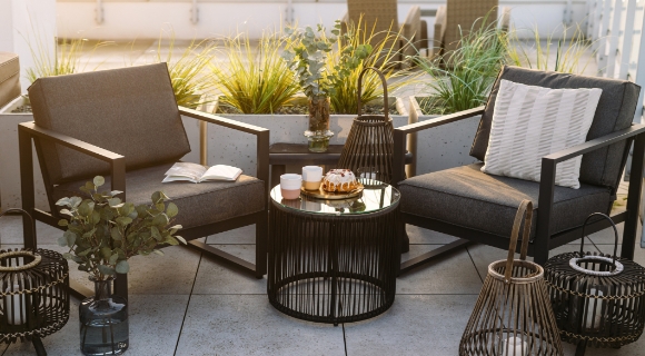 Zwei moderne Terrassenst&uuml;hle, ein Couchtisch und mehrere Laternen auf einem Balkon.