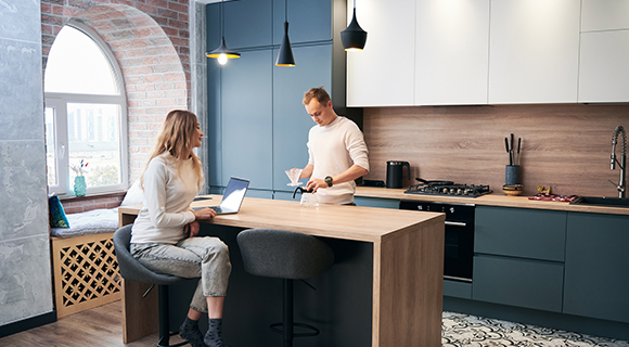 Zwei Personen in einer modernen Küche mit Kücheninsel, Hängelampen und großen Fenstern beim gemeinsamen Gespräch.