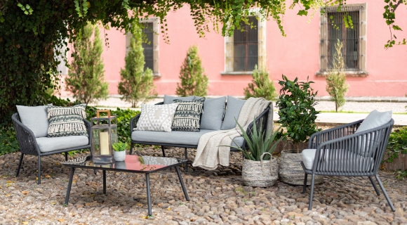 Outdoor Lounge mit grauen Webm&ouml;beln und stilvoll gemusterten Kissen auf einer Kopfsteinpflasterterrasse.