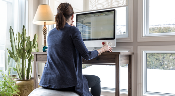 Frau sitzt im Homeoffice auf einem Sitzball am Schreibtisch.
