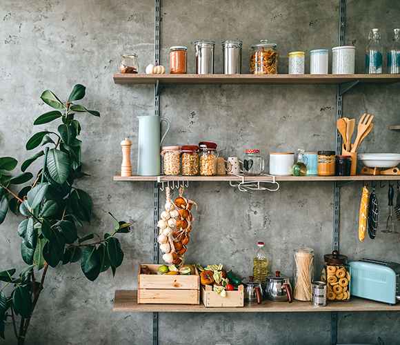 Offene Küchenregale mit Vorratsgläsern, Küchenutensilien und frischem Gemüse an Betonwand.